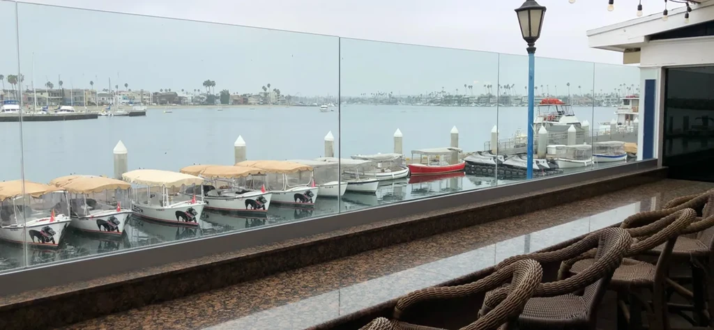 Outdoor restaurant overlooks overcast bay with boats, distant buildings, and palm trees.