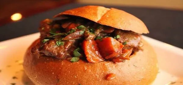 Close-up of a rustic meat and vegetable stew in a bread bowl.