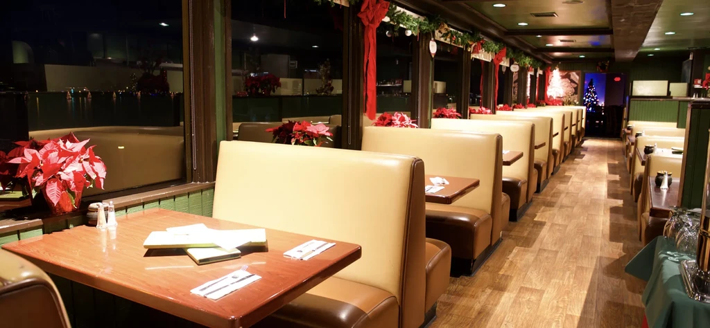 Empty restaurant dining area with booths, windows, tables, and Christmas decor.