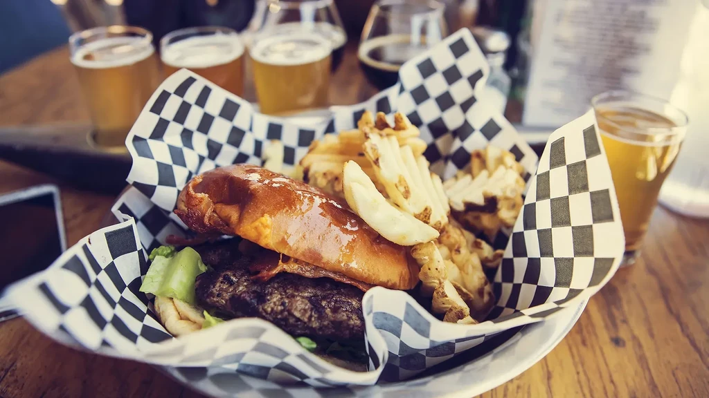 A gourmet burger, waffle fries, and a blurred beer flight on a table.