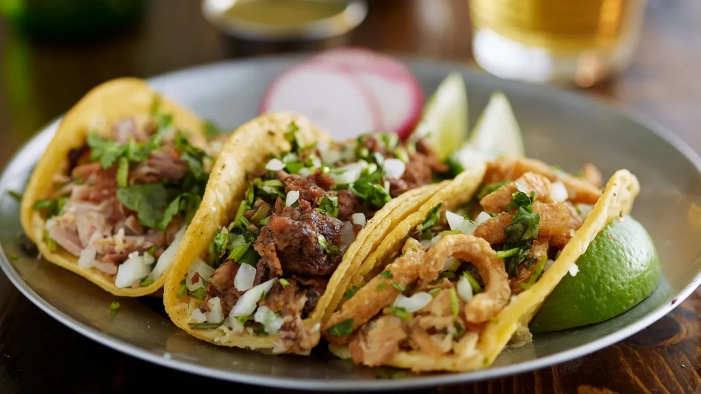 Three street-style tacos with meat, onion, cilantro, lime, and radish.