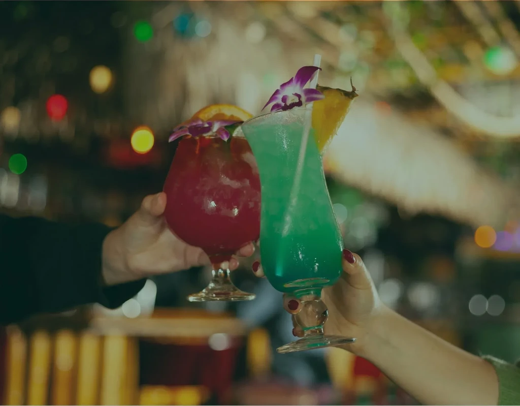 Two hands toast colorful tropical cocktails with orchids.