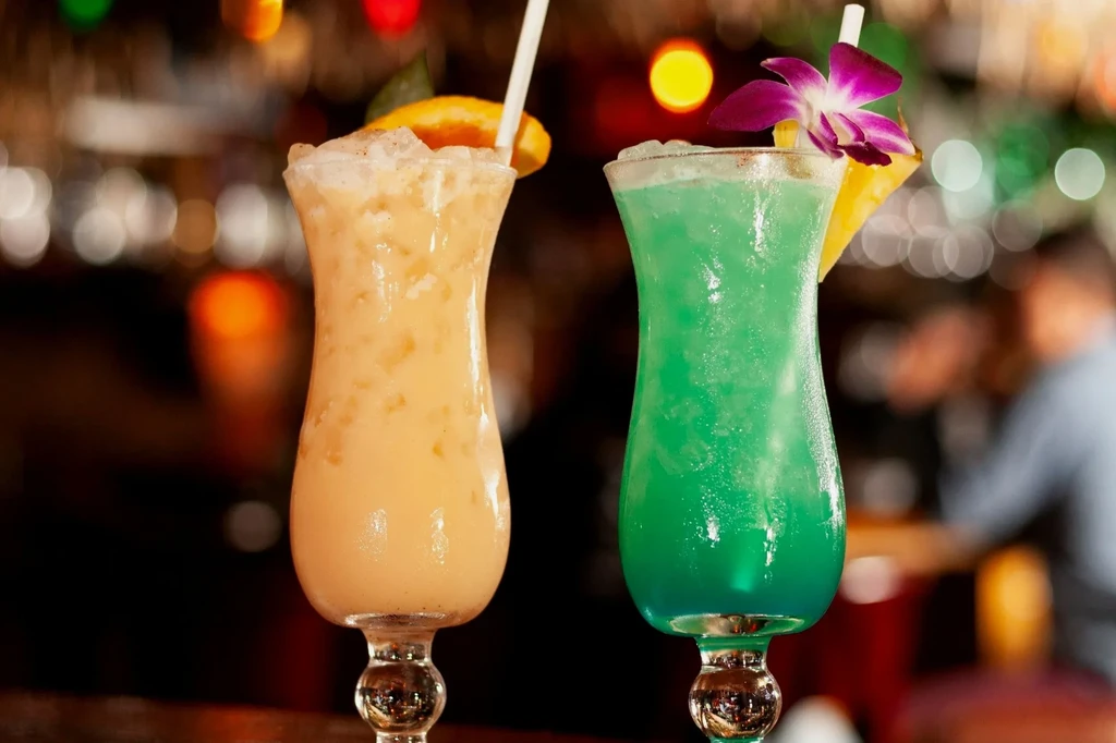 Orange-yellow and blue-green tropical cocktails, garnished with fruit and orchid.