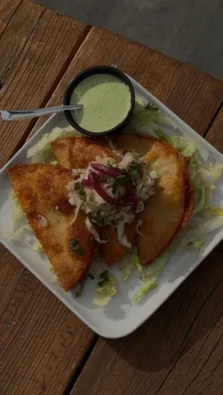 Plate of golden fried turnovers, cabbage slaw, pickled onions, and green sauce.