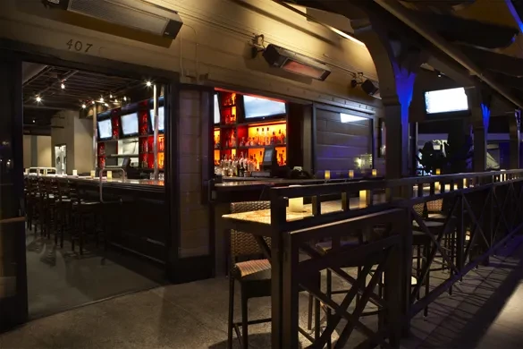 Modern bar and cool-lit patio at night with glowing liquor bottles.