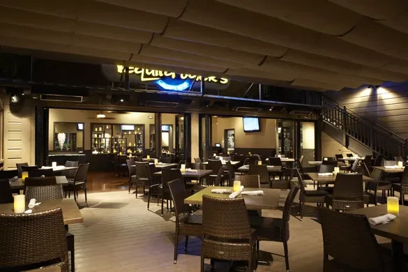 Nighttime restaurant patio with lit tables and a 'Tequila Works' neon sign.