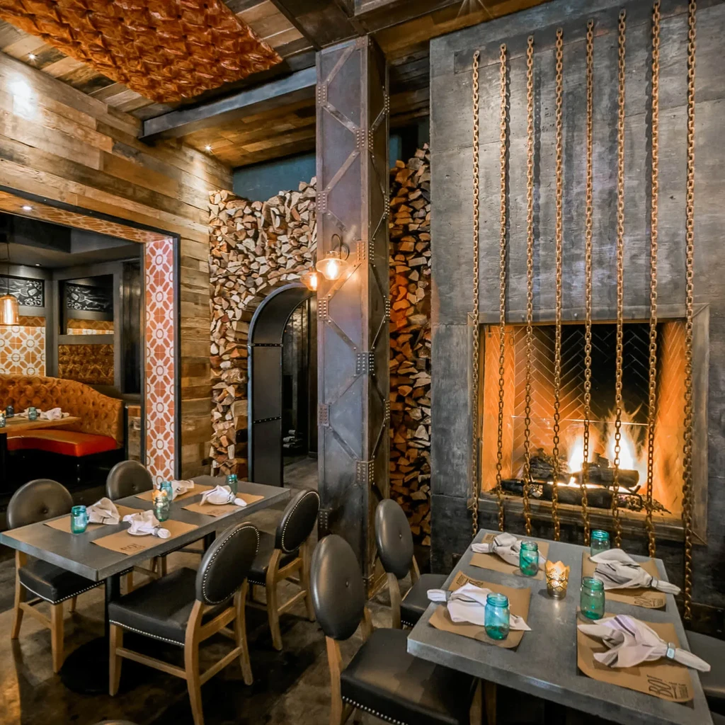 Rustic-industrial restaurant interior with large burning fireplace and wood decor.