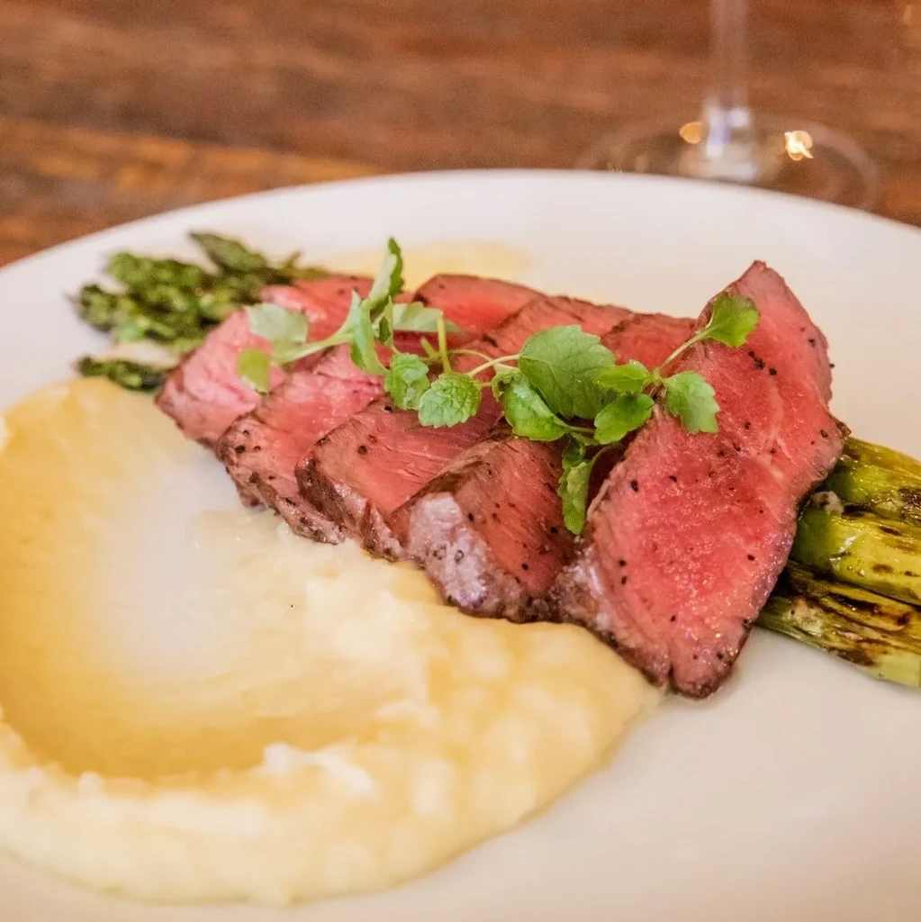 Slices of medium-rare steak, mashed potatoes, and asparagus on a plate.