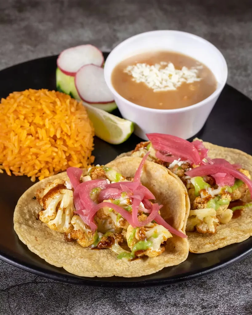 Roasted cauliflower tacos with rice, beans, and lime on black plate.