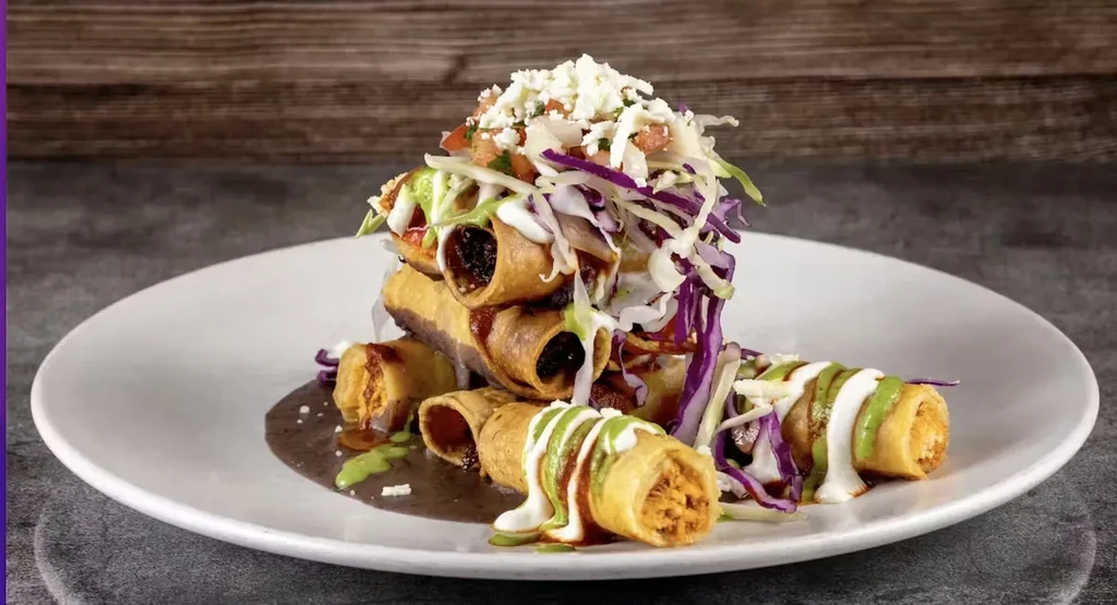 Vibrant taquitos with colorful cabbage, pico, cheese, crema, and sauces.