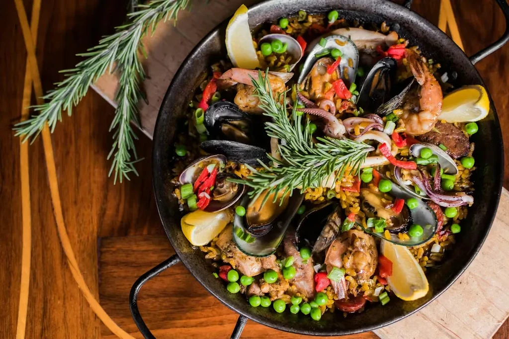 Overhead paella with seafood, chicken, vegetables, rice, rosemary, lemon.