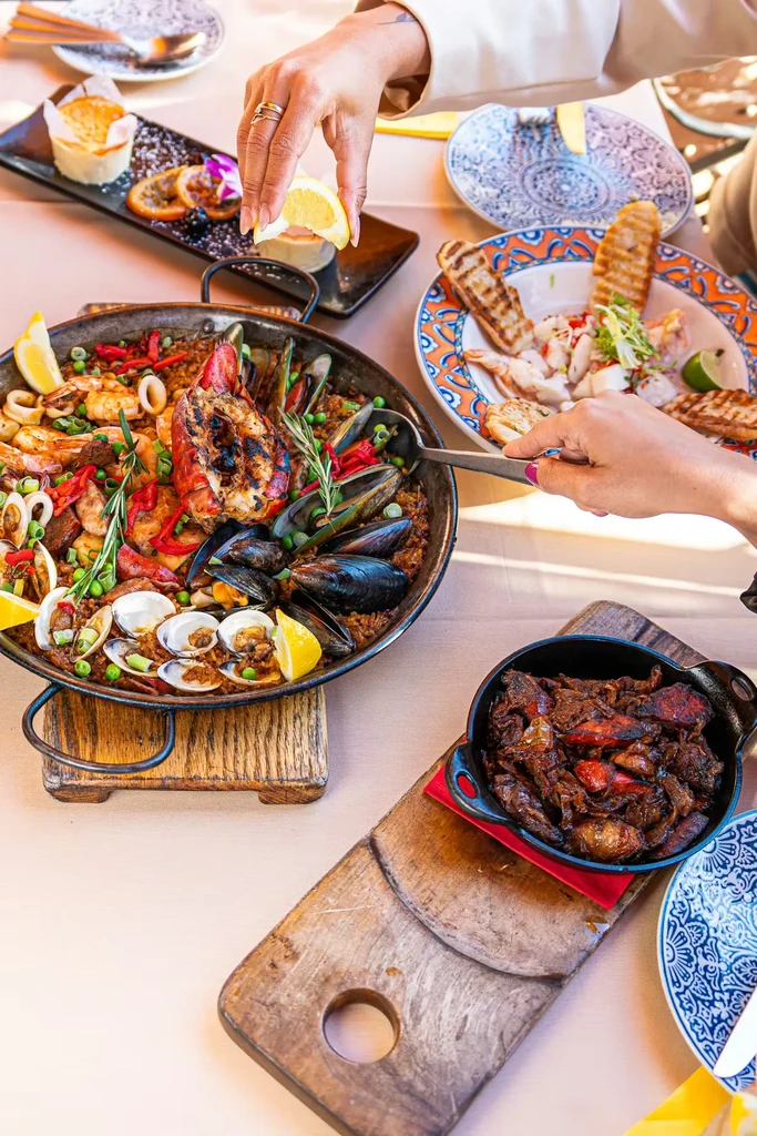 Hands serve seafood paella with grilled lobster and other dishes.