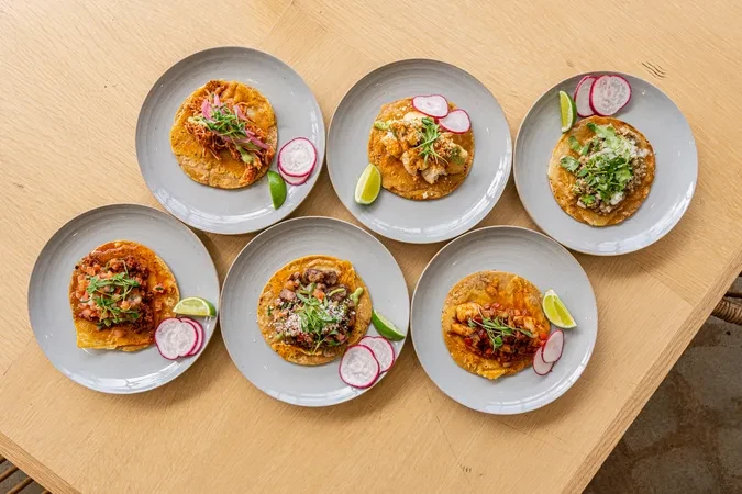 Six colorful tacos with various toppings on a wooden table.