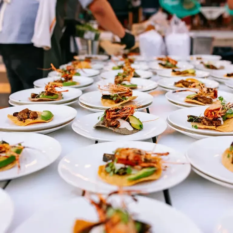 Precisely arranged individual shrimp appetizers with avocado; staff preparing more.