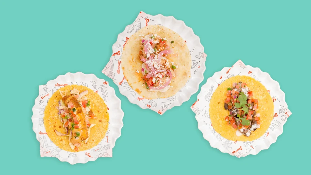 Overhead shot of three distinct, colorful tacos on a vibrant teal background.
