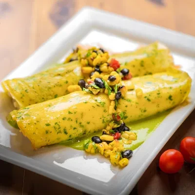 Two yellow rolls with green sauce, corn-bean salsa, and cherry tomatoes.