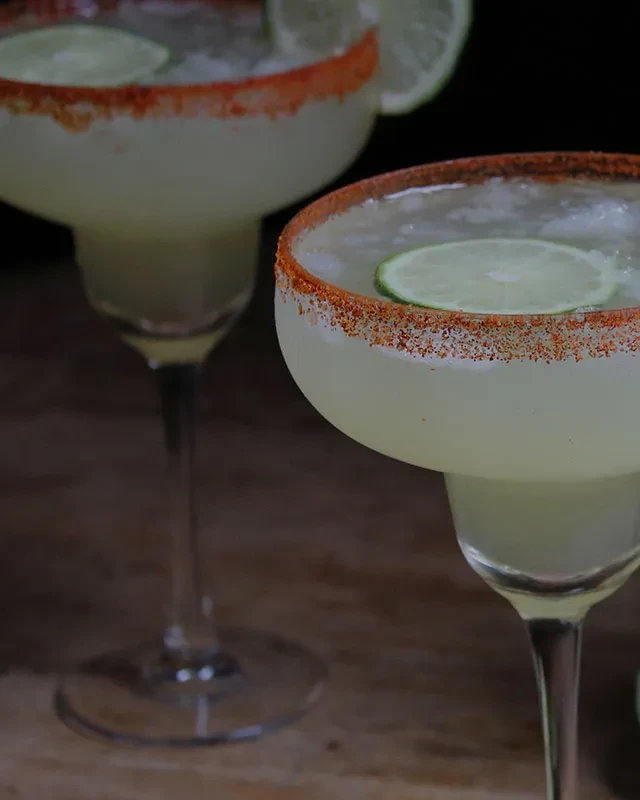 Frosted margarita-style drinks with chili-lime rims on wood.