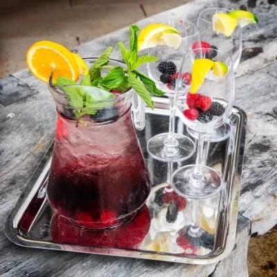 Pitcher of berry drink with mint, orange, and glasses on silver tray.