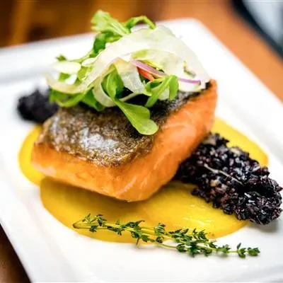 Plated pan-seared salmon with salad, yellow puree, black rice, and thyme.