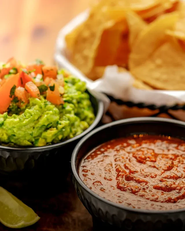 Close-up of vibrant guacamole, chunky salsa, lime, and tortilla chips.