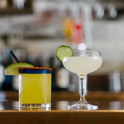 Chili-lime cocktail and cucumber cocktail on a bar surface.