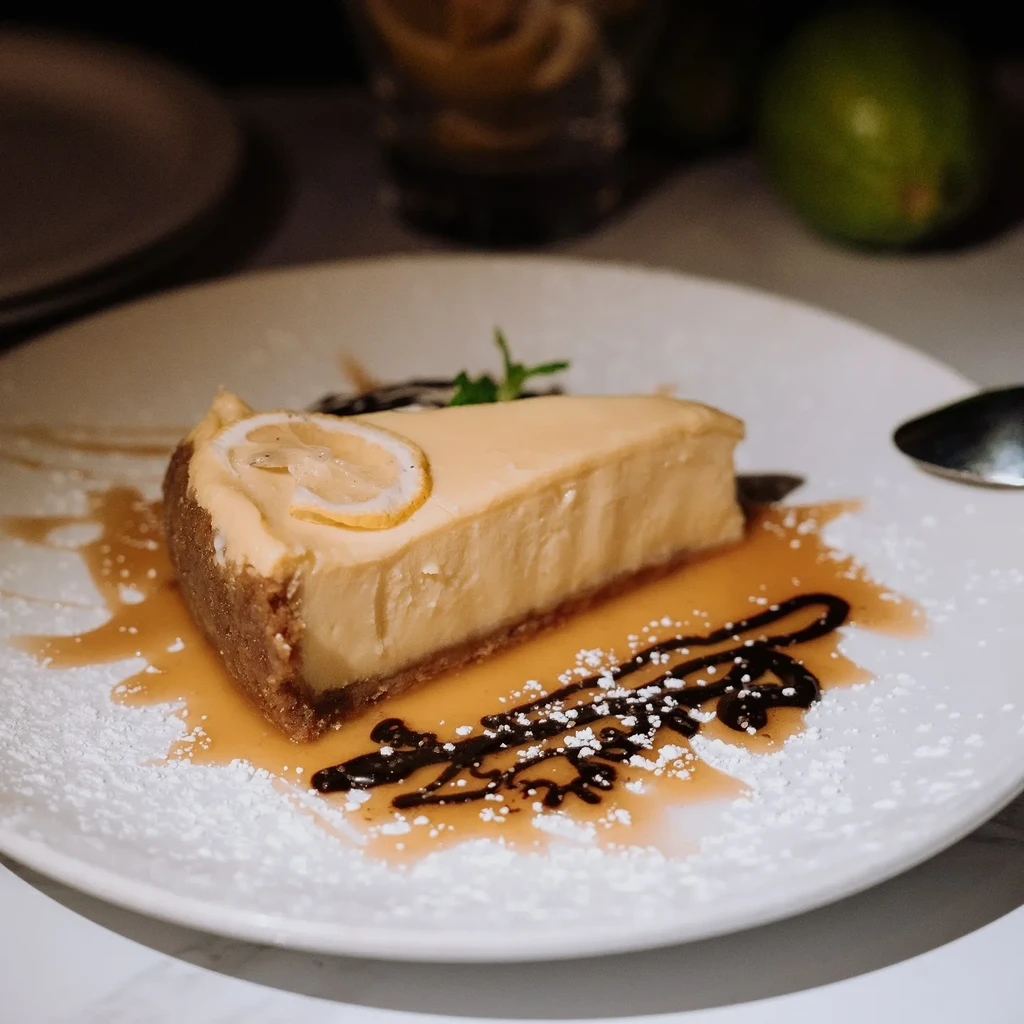 A slice of cheesecake with lemon, mint, caramel, and chocolate drizzles.