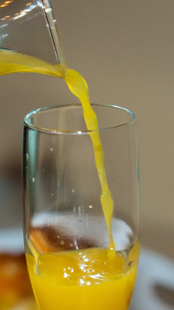 Close-up of yellow liquid pouring into a tall glass, splashing.