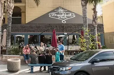 Lively outdoor scene at The Breakfast Bar with people, palms, umbrella.