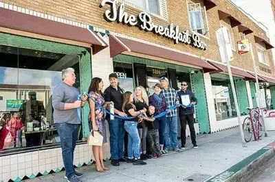 Group cuts blue ribbon at "The Breakfast Bar" grand opening.