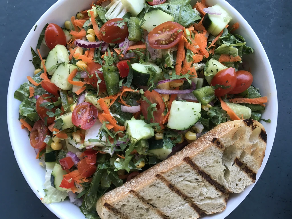 Close-up of a colorful salad with grilled bread in a white bowl.
