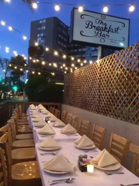 "The Breakfast Bar" outdoor dining table set with candles, string lights.