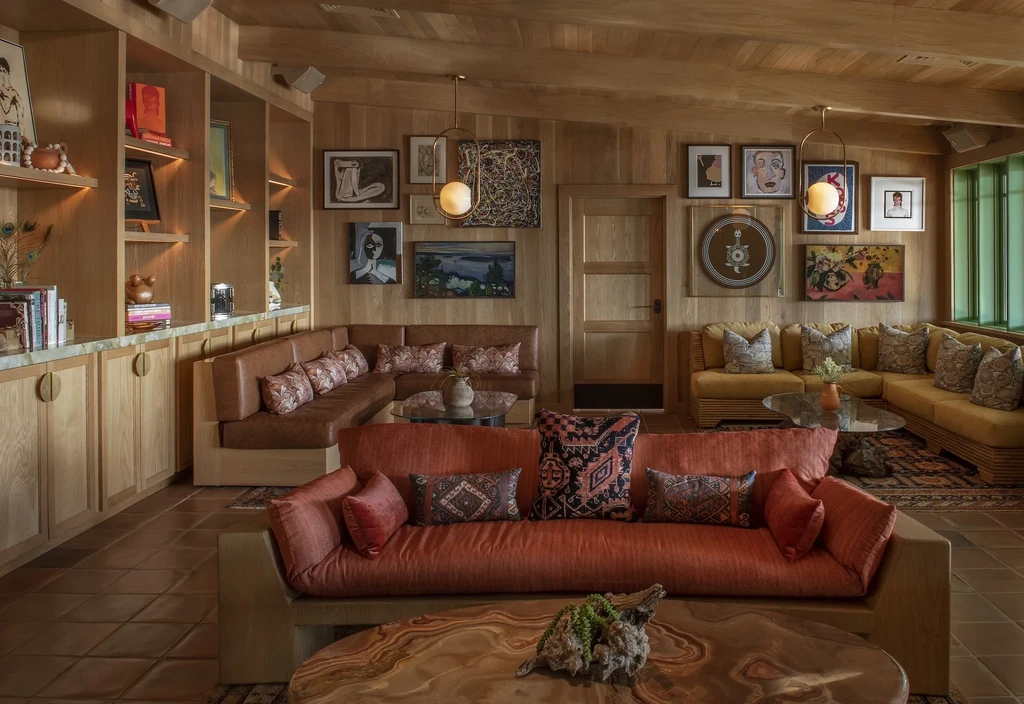 Warmly lit lounge with wood walls, terracotta floor, colorful sofas, and art.