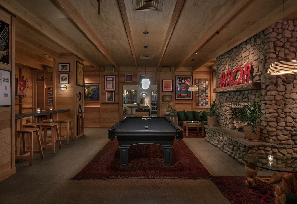 Rustic modern lounge with black pool table, stone fireplace, and green sofa.