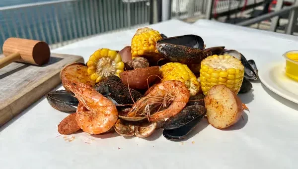 Outdoor seafood boil with shrimp, mussels, corn, potatoes, and mallet.