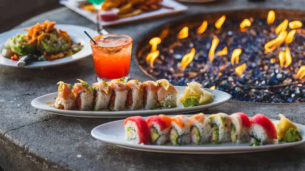 Two sushi plates, a cocktail, and a glowing outdoor fire pit.