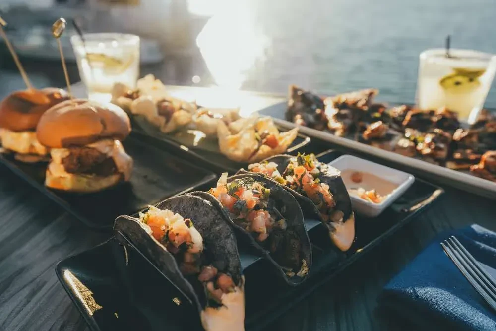 Sunlit waterfront dining featuring tacos, sliders, and drinks.