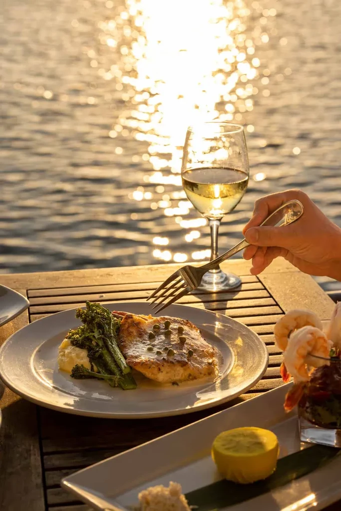 Golden hour outdoor dining with fish, white wine, shrimp, and fork.