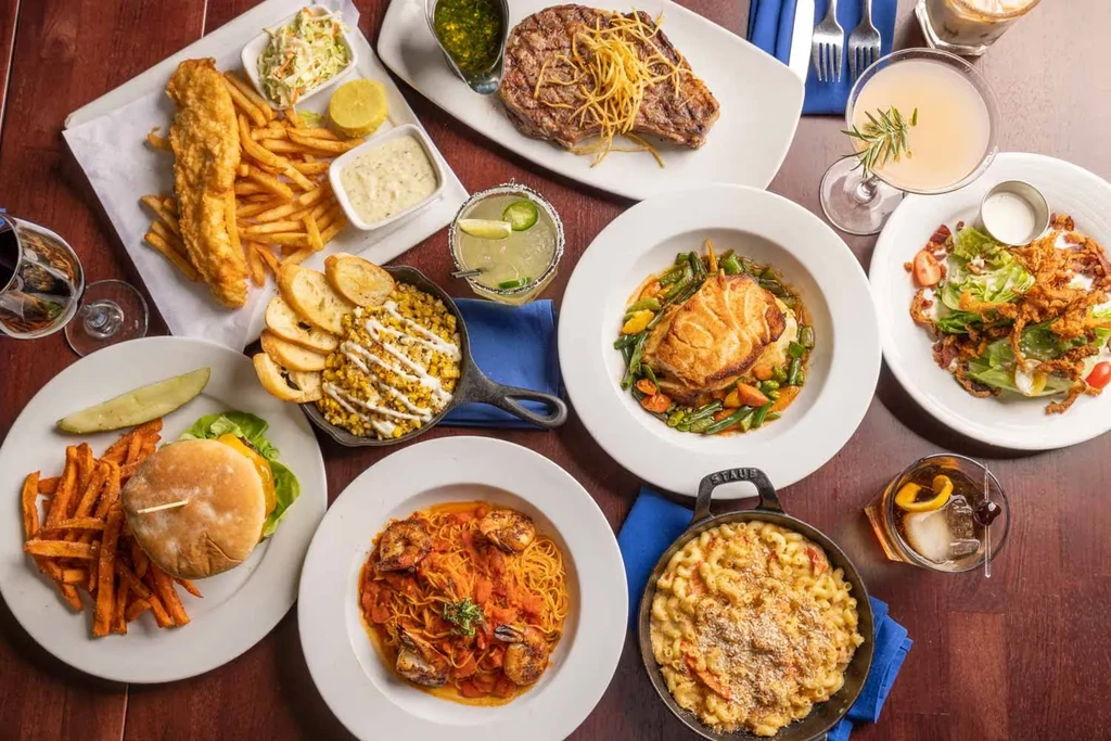 Overhead shot of many restaurant dishes and drinks on a dark table.