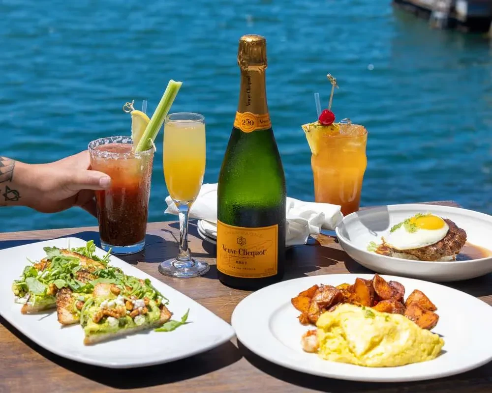 Waterfront dining with avocado toast, eggs, hamburger, and brunch drinks.