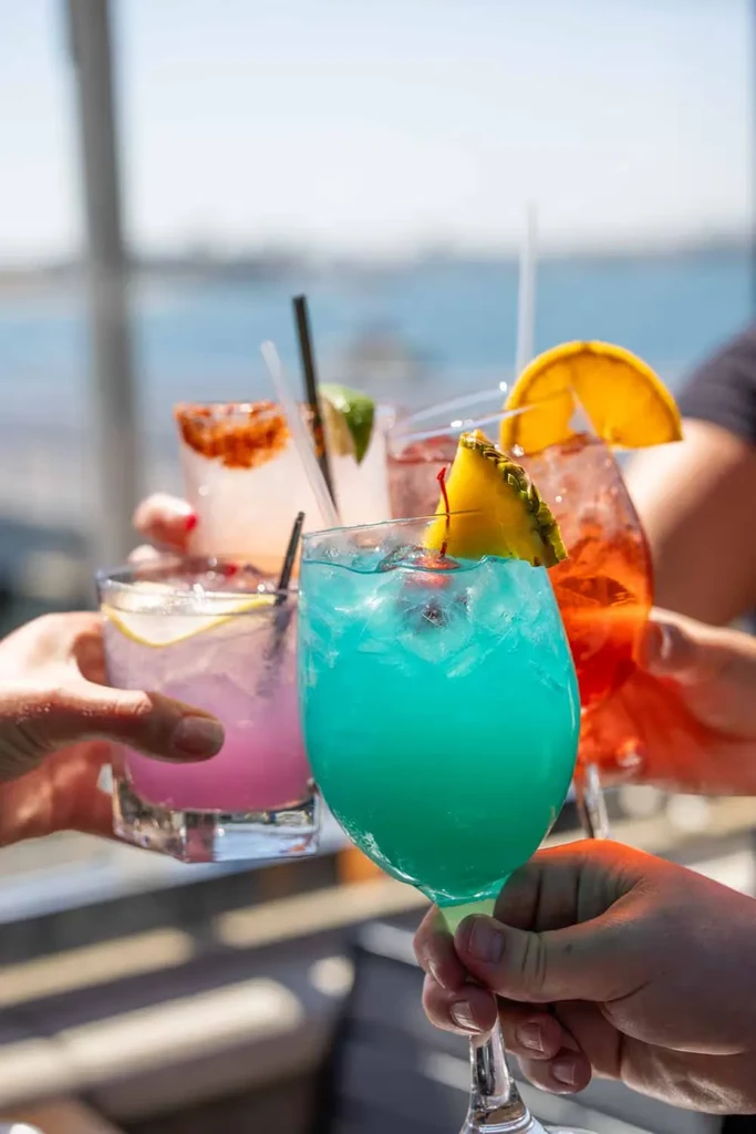 Five colorful cocktails with ice and garnishes, held up in a toast.