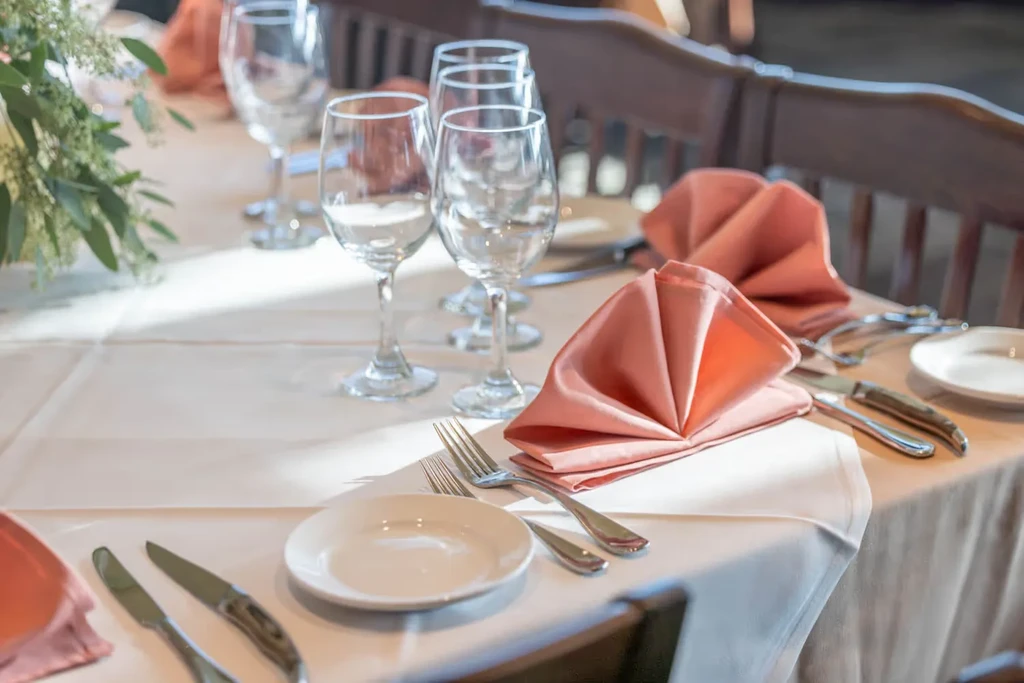 Restaurant table with white settings, peach napkins, and sparkling wine glasses.