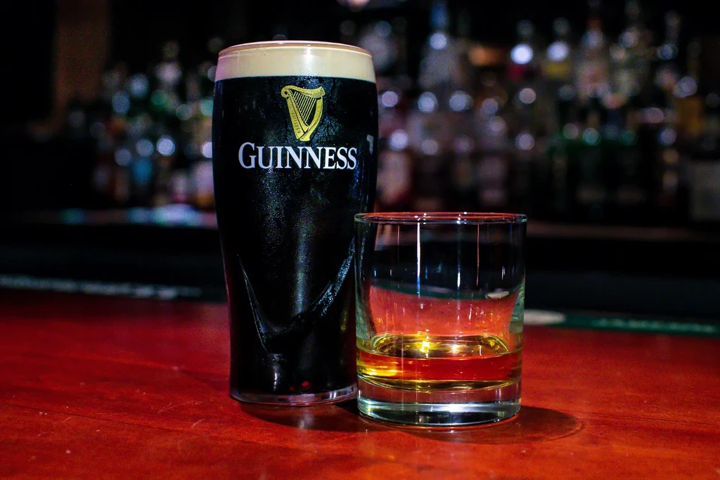 Guinness pint, whiskey glass, on a dark wooden bar.