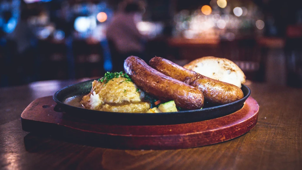 Sausages, mashed potatoes, vegetables, and herbs in a cast-iron skillet.