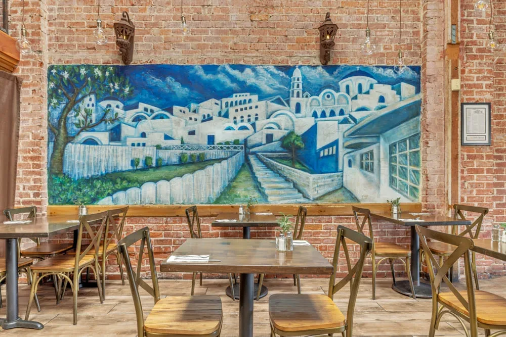 Vibrant Greek village mural on a brick wall in an empty restaurant.