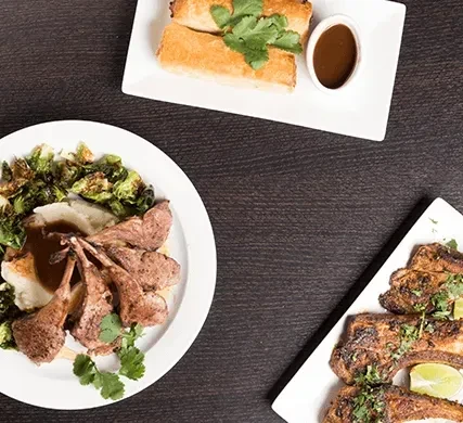 Top-down view of three restaurant dishes: lamb, rolls, and grilled meat.