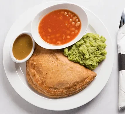 Golden pastry, mashed peas, baked beans, and gravy on a plate.