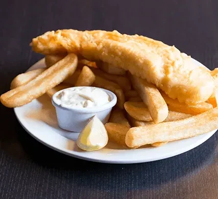 Close-up of golden battered fish, thick-cut chips, tartar sauce, and lemon.