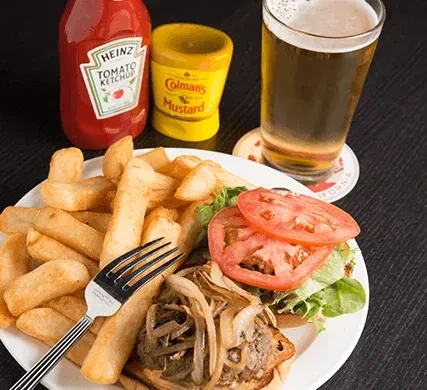 Overhead of open-faced burger, fries, beer, ketchup, and mustard.