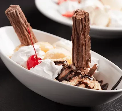 Ice cream sundae in boat bowl with cherry, chocolate, whipped cream.