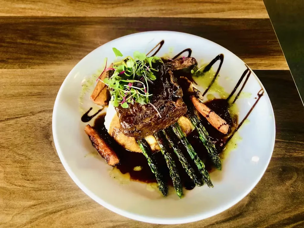 Plated gourmet dish: braised meat, purée, asparagus, carrots, and sauces.